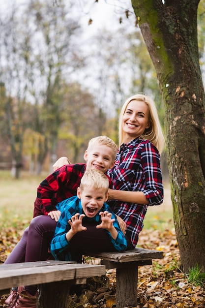 La famiglia bionda gioca su una panchina di legno nel parco autunnale, la madre abbraccia due gemelli maschi preadolescenti e sorride, un fine settimana attivo all'aperto
