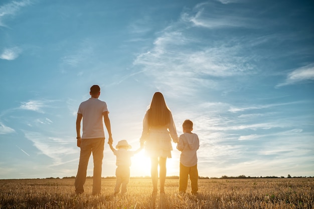 La famiglia con bambini cammina lungo i campi sul retro del tramonto