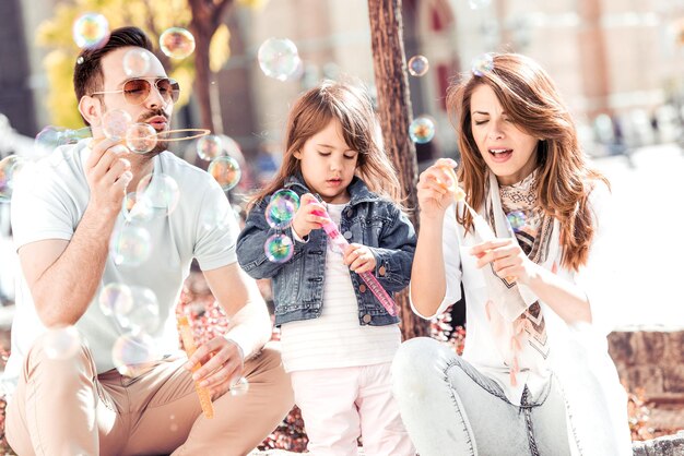 La famiglia con la figlia del bambino soffia le bolle di sapone all'aperto