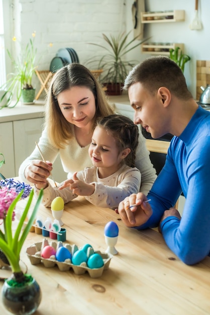 La famiglia dipinge uova di Pasqua colorate mamma papà e figlia festeggiano insieme le vacanze di primavera giovane donna uomo e ragazza colorando uno scenario tradizionale