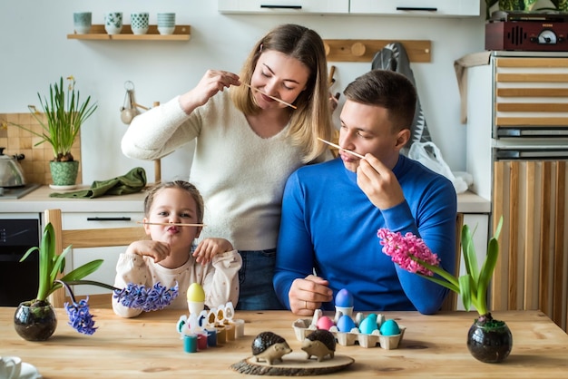 La famiglia dipinge uova di Pasqua colorate mamma papà e figlia festeggiano insieme le vacanze di primavera