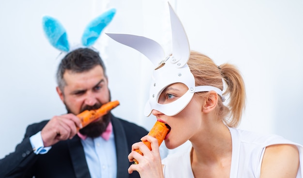 La famiglia divertente celebra la Pasqua. Conigli pasquali. Coppia di coniglietti. Buone vacanze. Le coppie con le orecchie del coniglietto stanno mangiando la carota.