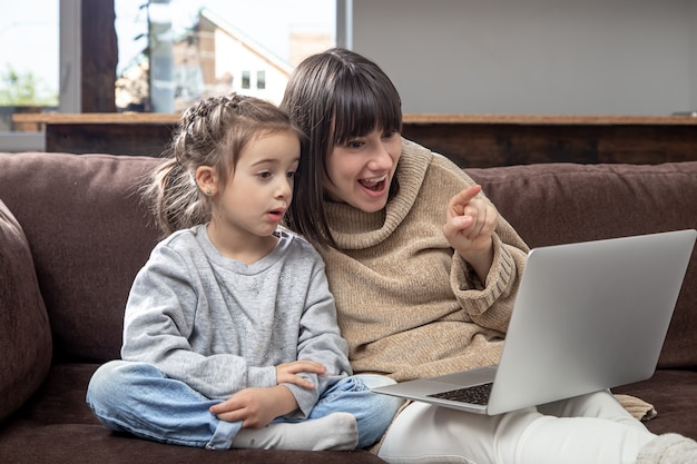 La famiglia felice che esamina lo schermo del laptop effettua la videochiamata a distanza. Madre sorridente e bambina che parlano alla webcamera sulla chat di Internet.