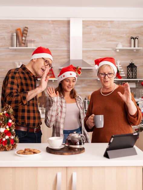 La famiglia felice che indossa il cappello di Babbo Natale saluta i genitori remoti che si godono le vacanze di Natale