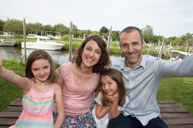 La famiglia felice che riposa insieme fa una foto selfie con lo smartphone all'aperto