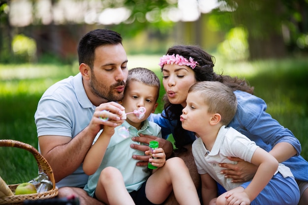 La famiglia felice con i bambini fa le bolle di sapone all'aperto