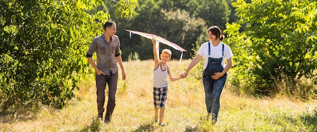 La famiglia felice con la moglie incinta fa volare un aquilone insieme nel campo estivo