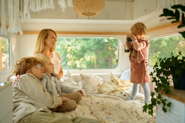 La famiglia felice dei campeggiatori posa in camper, campeggio estivo. Coppia con bambini viaggiano in auto da campo, interni del rimorchio sullo sfondo. Avventura in campeggio, stile di vita itinerante, vacanza in camper