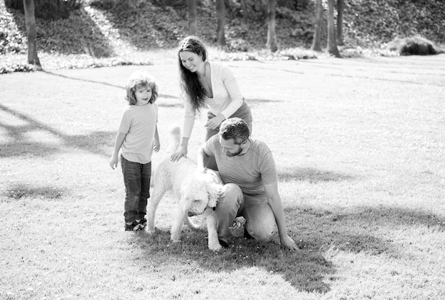 La famiglia felice di madre papà e figlio del bambino che gioca con il cane nell'erba verde del parco estivo si rilassa
