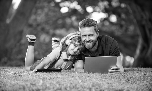 La famiglia felice di papà e figlio usa il laptop per videochiamate o lezioni ascolta musica in cuffia nella felicità del parco