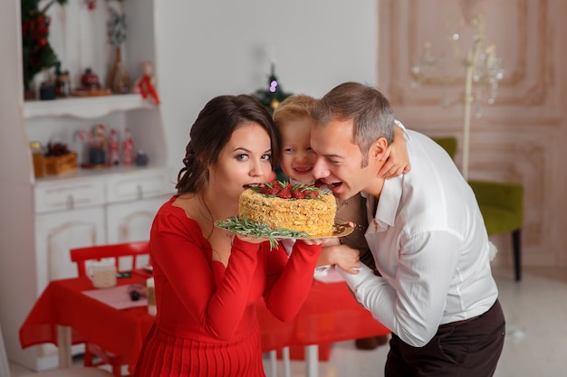 La famiglia felice morde una gustosa torta di Natale sulla cucina di fondo. Vacanze di Capodanno e divertimento.