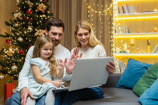 La famiglia felice saluta gli amici tramite video chat marito moglie e figlia seduti sul divano di casa e