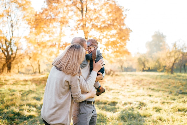 La famiglia felice si diverte con il loro adorabile bambino nel soleggiato parco autunnale.