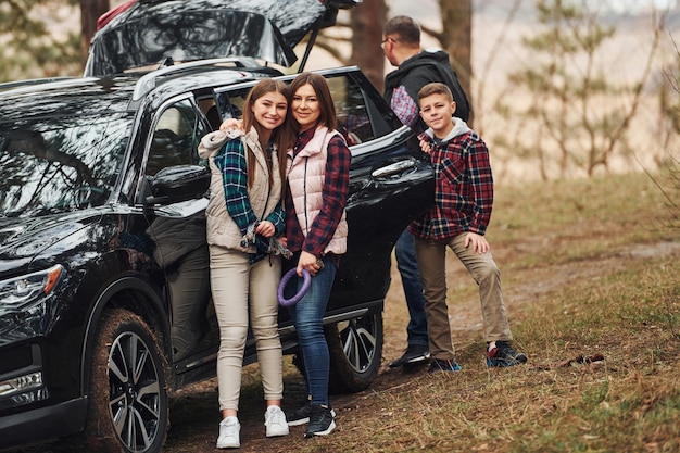 La famiglia felice si diverte con il proprio cane vicino a un'auto moderna all'aperto nella foresta