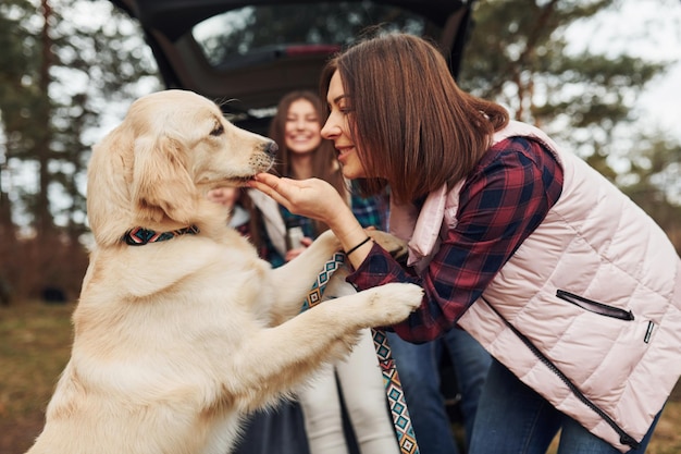 La famiglia felice si diverte con il proprio cane vicino a un'auto moderna all'aperto nella foresta