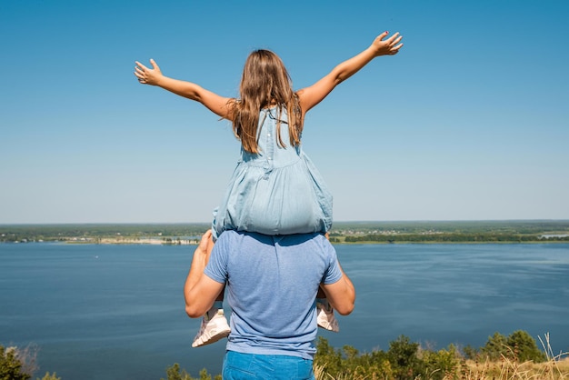 La famiglia felice si diverte e gioca in natura Il bambino si siede sulle spalle del padre Vista posteriore