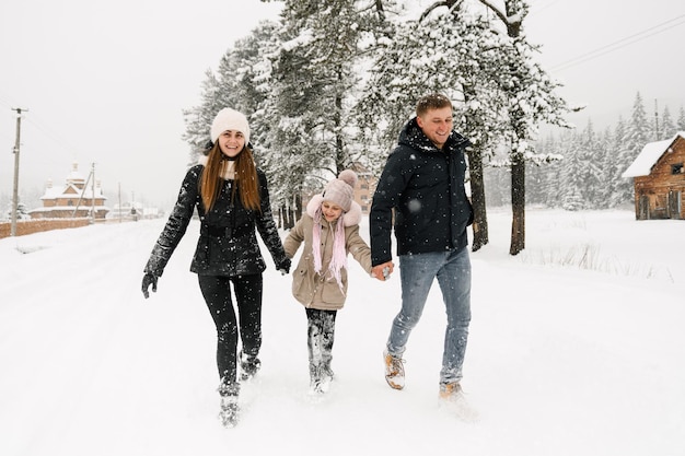 La famiglia felice si diverte nella foresta invernale. Madre, padre e figlia che giocano con la neve. Divertirsi a passare del tempo insieme. concetto di famiglia