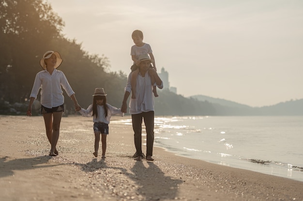 La famiglia felice si diverte sulla spiaggia al tramonto Padre, madre e bambini che giocano insieme