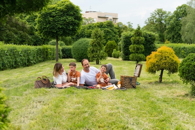 La famiglia felice si trova sull'erba durante un picnic nel parco, c'è un cestino con cibo e giocattoli