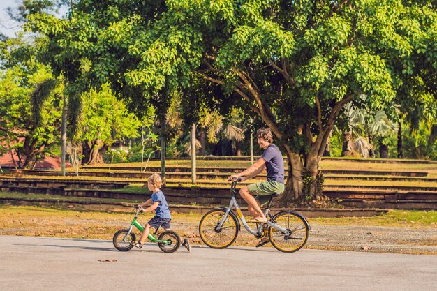 La famiglia felice sta andando in bicicletta all'aperto e sorride. Padre in bici e figlio in bici senza pedali