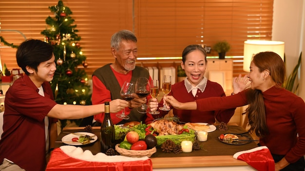 La famiglia felice sta facendo tintinnare un bicchiere di vino durante la celebrazione della cena della festa di Natale Natale e concetto di ringraziamento