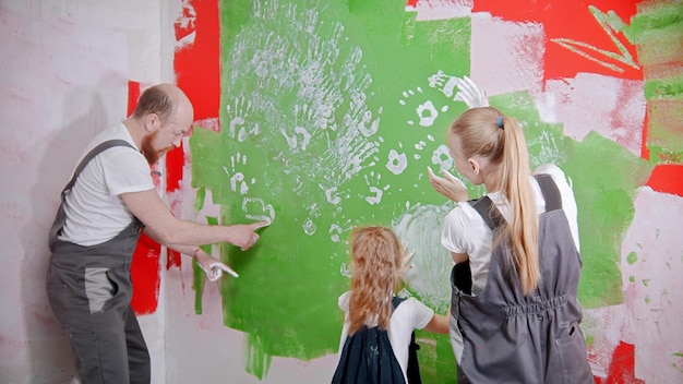 La famiglia felice sta mettendo le sue impronte bianche su un muro verde papà disegna qualcosa sul muro