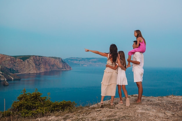 La famiglia felice sul bordo della scogliera gode della vista sulla roccia della cima della montagna al tramonto