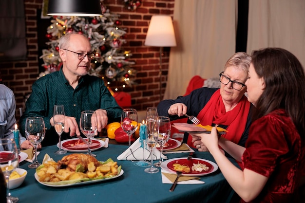 La famiglia festeggia il natale, cena festiva, passa un piatto con spuntini, piatto principale a tavola. Celebrazione delle vacanze invernali di Natale con i genitori in un bellissimo posto decorato