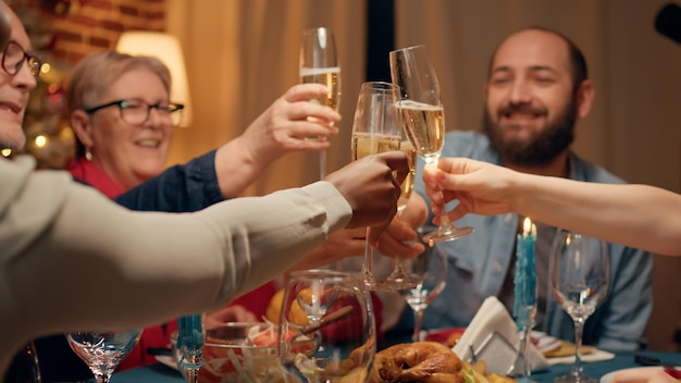 La famiglia festosa si è riunita a casa per festeggiare il Natale mentre brinda allo spumante nella sala da pranzo. Persone diverse e positive che celebrano le vacanze invernali con cibo tradizionale cucinato in casa.