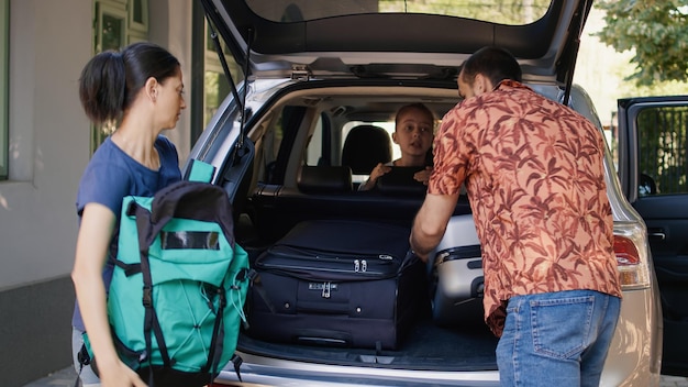 La famiglia si prepara per la gita estiva mentre carica il veicolo con i carrelli da viaggio e il citybreak. I genitori mettono i bagagli nel bagagliaio dell'auto mentre la figlia non paziente li affretta.