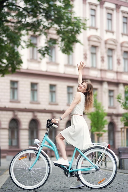 La fanciulla felice si gode un giro in bicicletta per le strade della città sullo sfondo di un edificio architettonico a molti piani