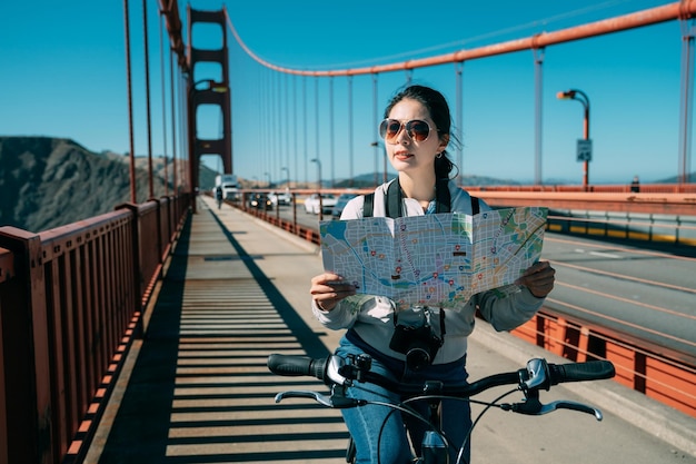 la femmina asiatica che viaggia in bicicletta al Golden Gate Bridge è alla ricerca di indicazioni stradali con una mappa a San Francisco in California in una giornata di sole in estate.