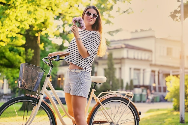 La femmina castana tiene il mazzo vicino alla bicicletta della città in un parco estivo.