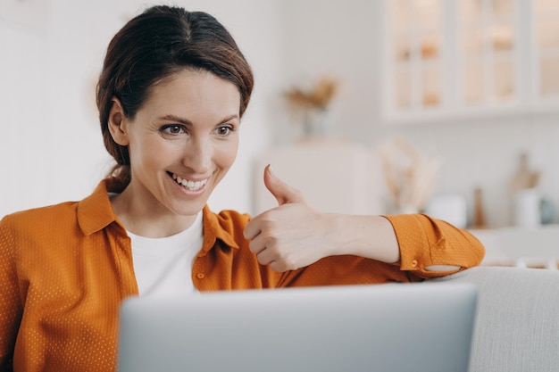 La femmina mostra il gesto del pollice in su guardando lo schermo del laptop consiglia che il servizio online effettua una videochiamata