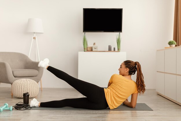 La femmina nera che fa la gamba laterale solleva l'allenamento sdraiato a casa