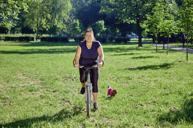 La femmina positiva del corpo va in bicicletta nel giardino della città durante il giorno