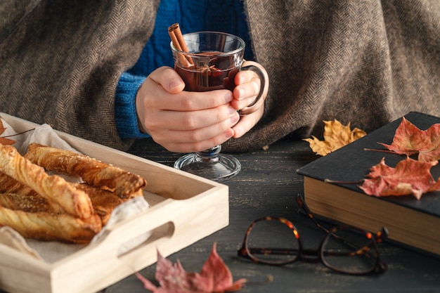 La femmina si siede a casa con la bevanda calda nella stagione autunnale