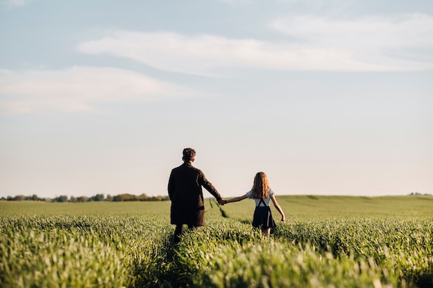 La figlia adolescente cammina con suo padre in un prato tenendosi per mano la sera.