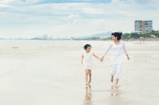 La figlia asiatica felice della famiglia e della madre della famiglia funziona, ridendo e gioca alla spiaggia.