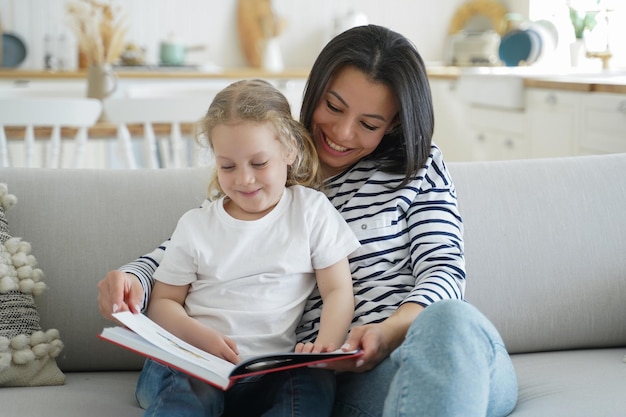 La figlia prescolare della mamma ha letto il libro insieme rilassandosi sull'accogliente divano godendosi il tempo libero insieme a casa