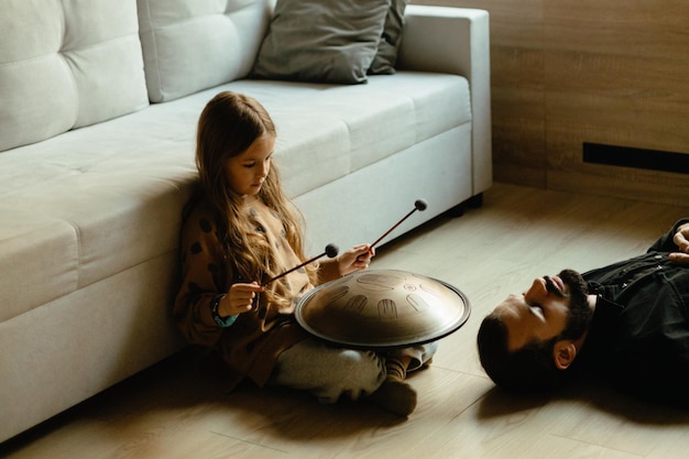 la figlia suona il handpan per suo padre che si sta rilassando sul pavimento dell'appartamento