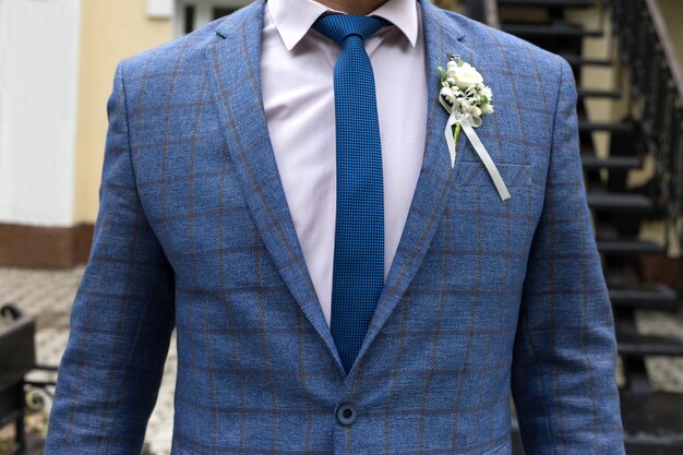 La figura di un uomo in giacca blu con cravatta blu e boutonniere bianco, senza volto