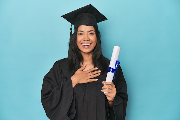 La filippina laureata con diploma sullo studio blu ride ad alta voce tenendo la mano sul petto