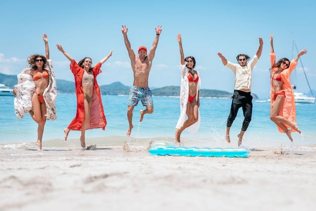 La folla degli amici che saltano sulla spiaggia sabbiosa con le loro armi si è alzata contro il fondo del mare