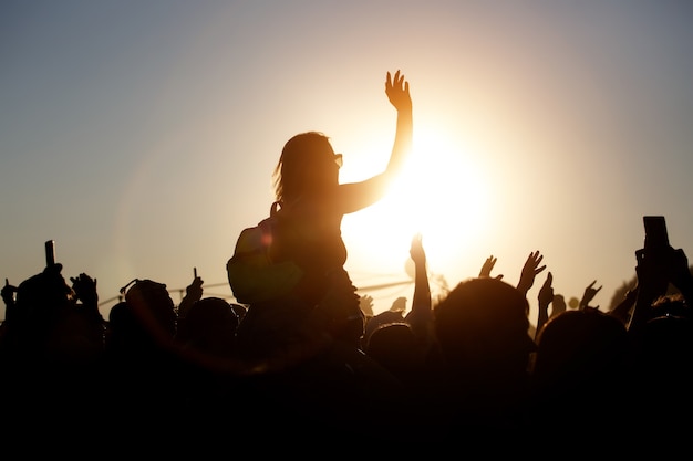 La folla si gode il festival musicale estivo, il tramonto, le sagome nere con le mani in alto, la ragazza al centro