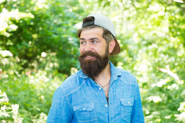 La folta barba è fantastica Ragazzo caucasico felice con la barba su sfondo naturale Uomo barbuto sorridente con baffi alla moda e forma della barba Pantaloni a vita bassa non rasati con barba testurizzata in estate all'aperto