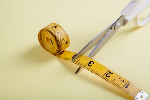 La forbice taglia il nastro di misurazione su sfondo giallo