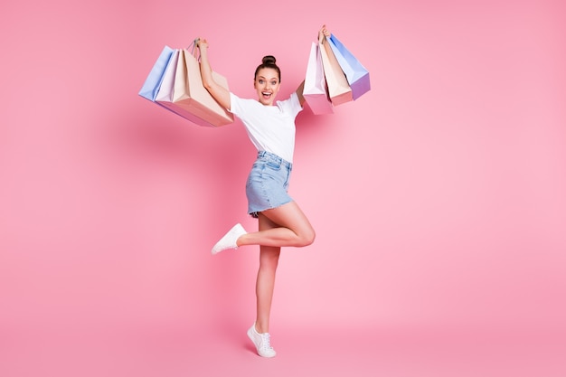 La foto a figura intera di una ragazza allegra positiva si diverte a fare shopping sollevando molte borse