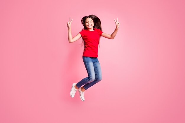 La foto a grandezza naturale di una ragazza allegra che salta fa sì che il segno V indossi abiti in stile casual isolati su uno sfondo di colore pastello