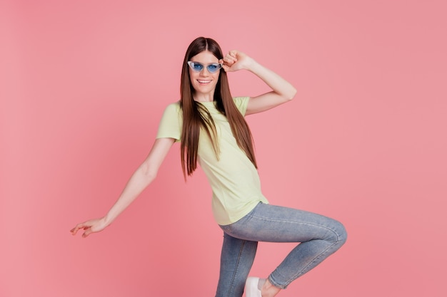 La foto a lato del profilo di una giovane donna felice sorriso positivo si diverte con gli occhiali da sole isolati su uno sfondo di colore rosa